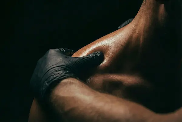 Primer plano intenso de pulgar de terapeuta aplicando presión precisa de masaje de tejido profundo en el músculo del hombro para liberación estructural. Estilo clínico OMAIA