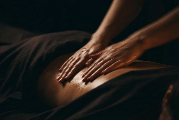 Primer plano oscuro de manos de terapeuta realizando un masaje de terapia fluida y relajante en la espalda para desconexión profunda. Estilo clínico de lujo OMAIA.